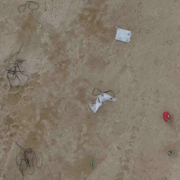 Drohnenaufnahme eines sandigen Testgeländes, auf dem verschiedene Strandmüllobjekte wie Plastikplanen, Bojen und Kanister verteilt sind.  