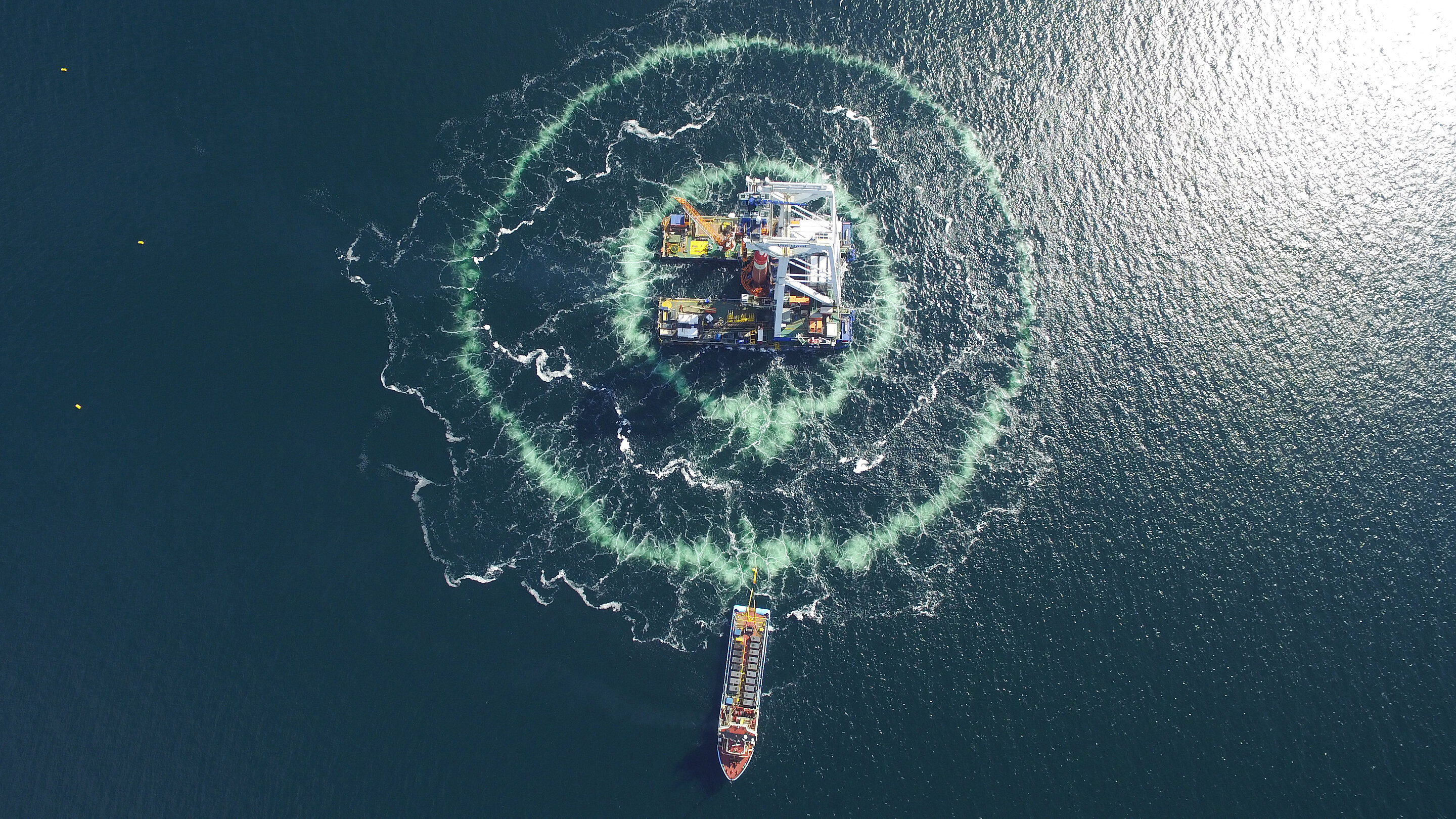 Luftaufnahme einer Rammplattform für Offshore-Windenergieanlagen, die von einem doppelten Blasenschleier umgeben wird.