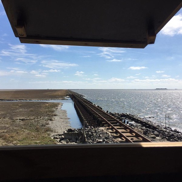 View out of the window of a high seat onto the embankment with the rails, On the right side the sea, on the left salt marshes.