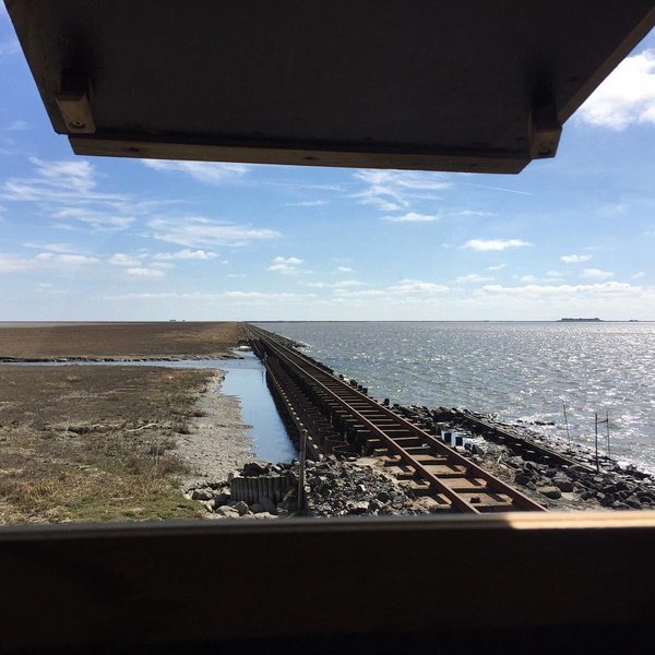 Blick aus dem Fenster eines Hochsitzes auf den Damm mit den Schienen, Auf der rechten Seite das Meer, links Salzwiesen.