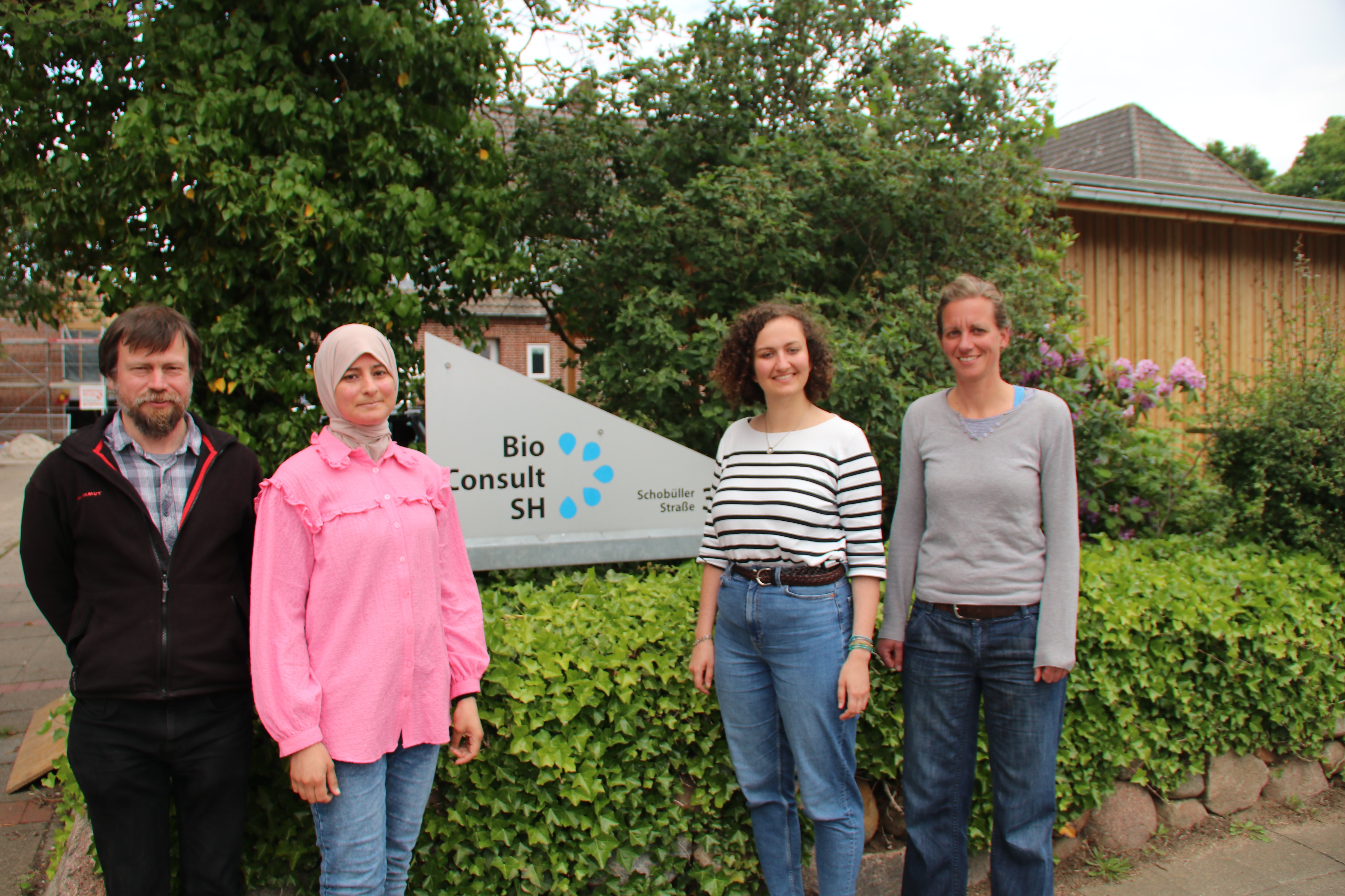 Vier Menschen stehen vor dem Firmenschild der Firma BioConsult SH.