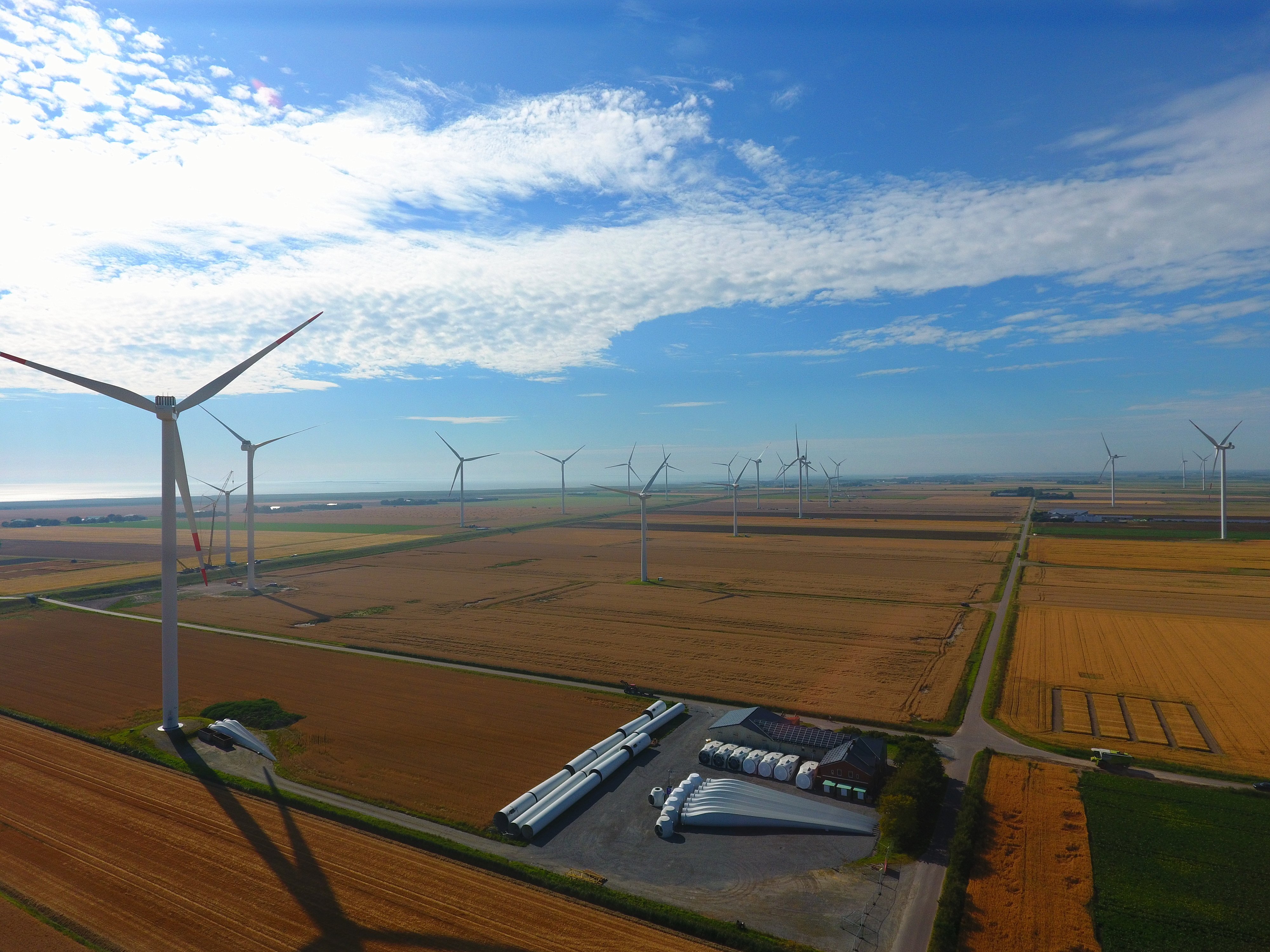 Aerial view of fields on which wind turbines are located. Components for wind turbines are stored in the foreground.