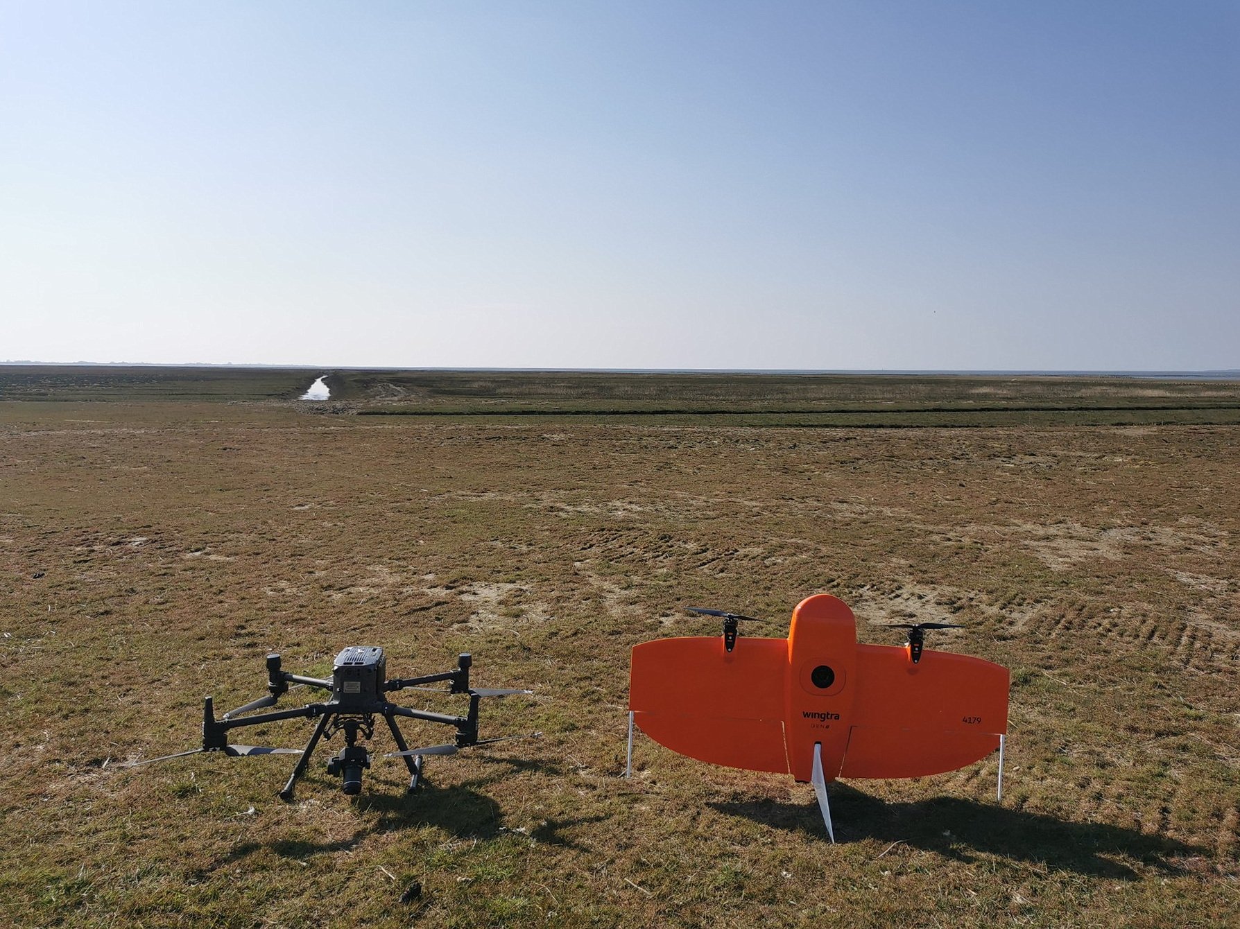 Two drones (DJI Matrice 300 RTK and Wingtra GEN II) are ready for use in a salt marsh.