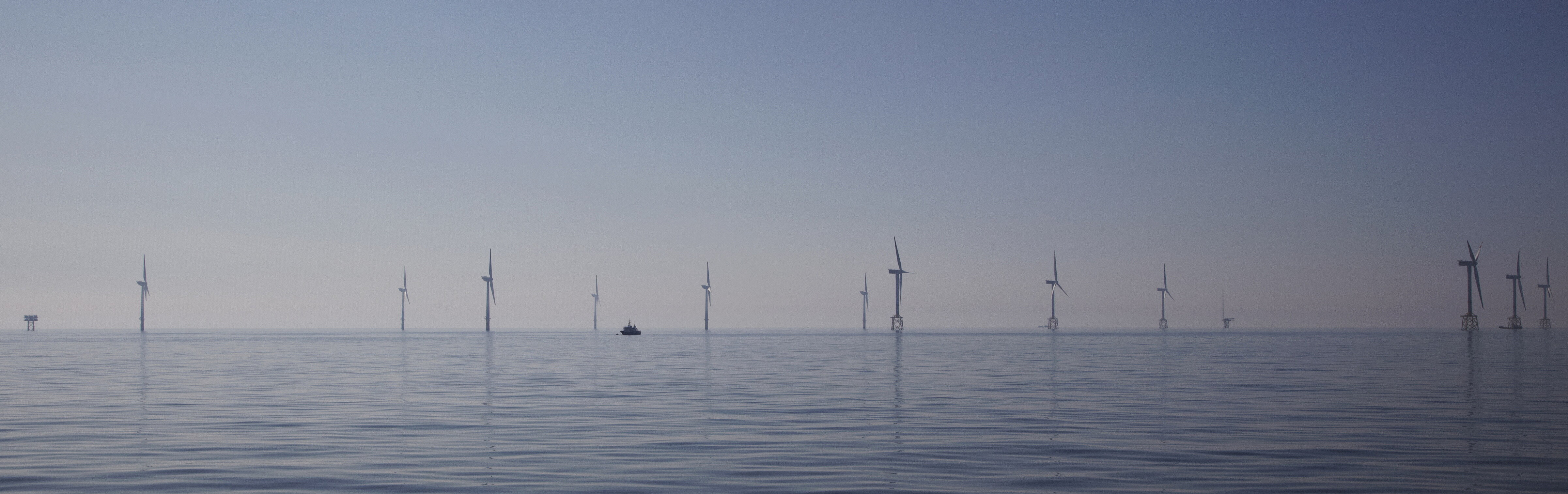 Stilles Wasser auf dem Meer, in einiger Entfernung ein Windpark.