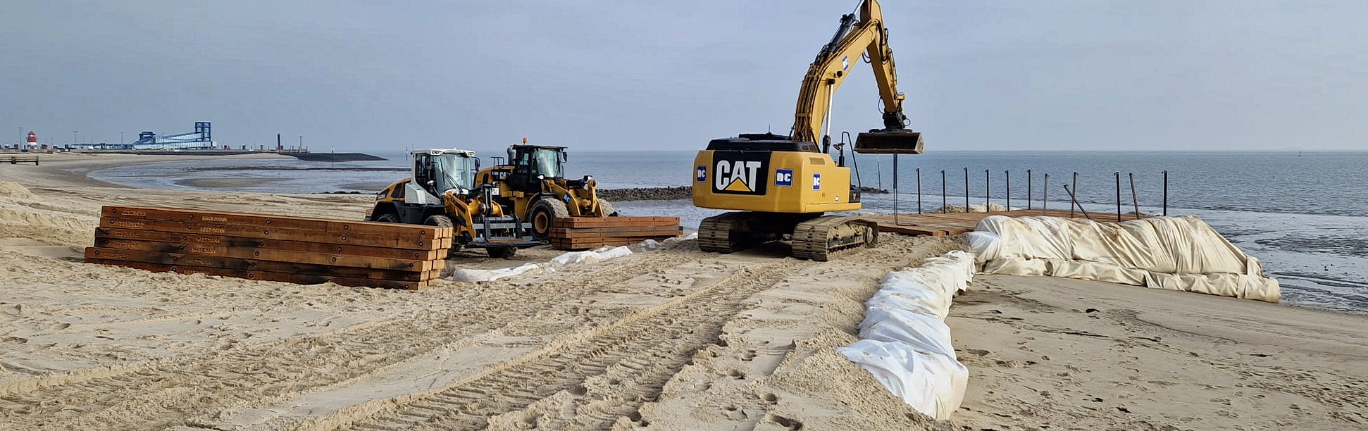 Zwei Radlader und ein Bagger im Einsatz auf einer Baustelle am Strand.