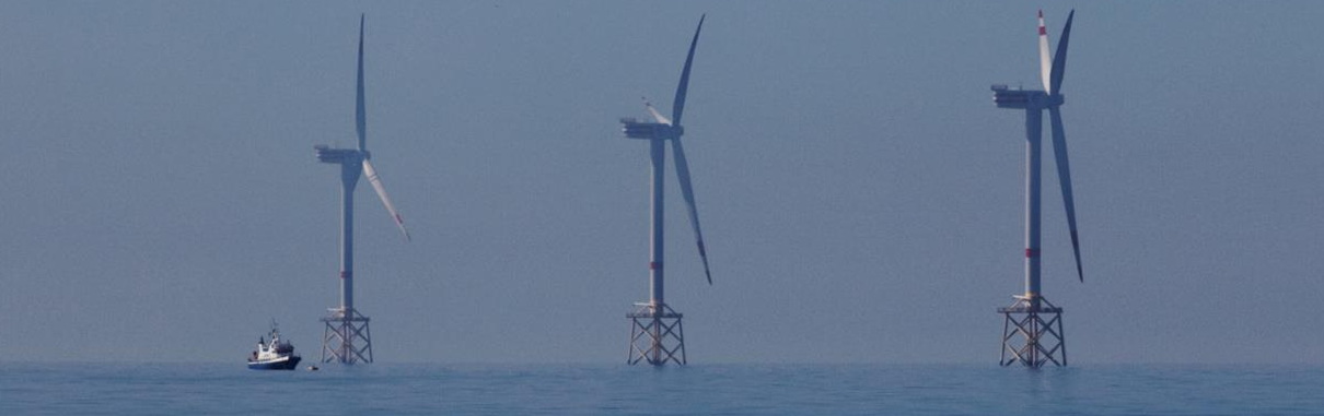 Three wind turbines on the high seas, a ship anchored to the left.